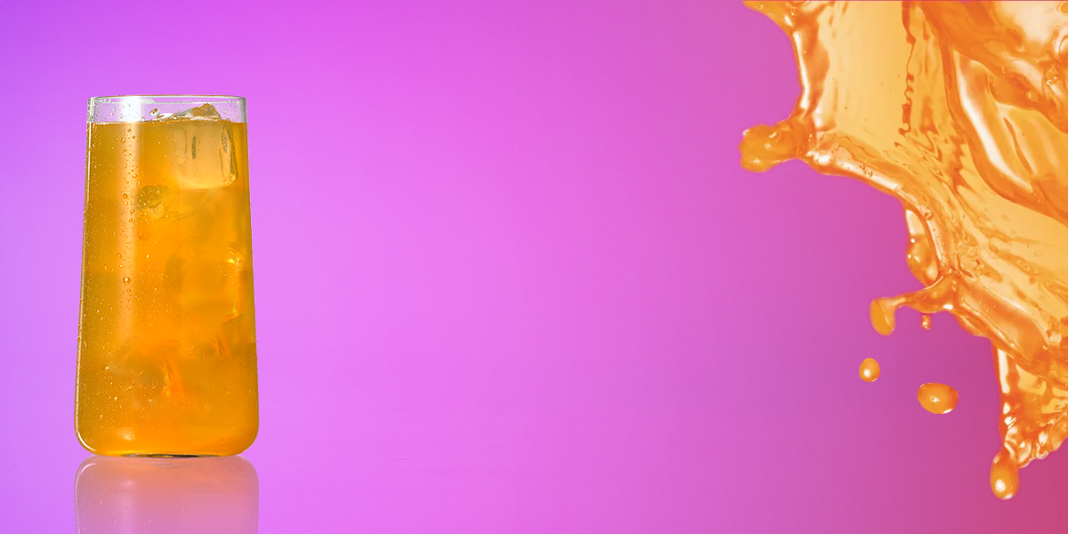 vaso con hielo lleno de jugo color naranja de sabor a tropical punch. A su lado un splash de jugo.