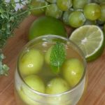 Vaso de cristal con bebida clara, uvas verdes frescas y hojas de menta.
