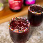 Vasos con bebida oscura de uva y bordes decorados con grajeas de colores brillantes.
