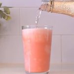 Sirviendo una bebida espumosa color rosa en un vaso alto de cristal.